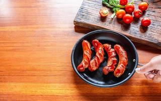 Fried sausage in a black pan in chef hands. photo