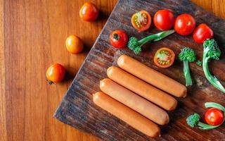 salchicha cruda en una tabla de cortar de madera con brócoli y tomates foto