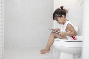 niño sentado en el inodoro sosteniendo la tableta.concepto de teléfono inteligente adicto al niño foto