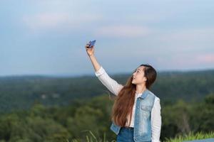 dama de buen humor con una sonrisa expansiva disfrutando de los fines de semana y tomando selfie en el teléfono móvil en la montaña foto