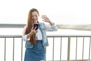 Portrait of young beautiful woman relax say hi wave hand live stream zoom in bridge. Smile happy fun caucasian girl relaxing smartphone, technology connection network, university lifestyle. photo