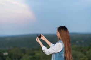 retrato de vista trasera de una mujer tomando una foto de un paisaje con un teléfono inteligente