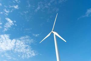 molino de viento o también turbina eólica en un parque eólico en rotación para generar energía eléctrica al aire libre con sol y cielo azul, concepto de conservación y energía sostenible foto