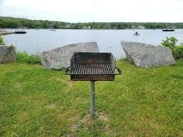 barbecue grill in grass near lake with boats and rocks photo