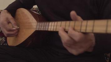 authentieke instrument-baglama. close-up op de vinger op een prachtig verlicht riet uitgevoerd door een jonge man. een snaarinstrument bespelen. bas spelen. video