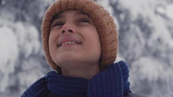 bambino che guarda in giro in una giornata di neve. ragazzo felice in abiti invernali guardandosi intorno in una giornata nevosa. video