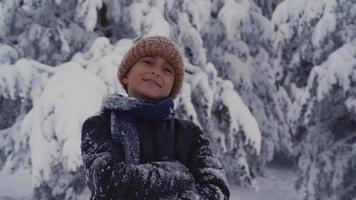 menino em tempo de neve, olhando ao redor. menino bonito com roupas de neve está olhando para a vista e cruzando os braços.