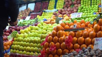 oranges, pommes et autres fruits. les commerçants placent des pommes dans l'allée. les oranges et les pommes vertes ressortent.