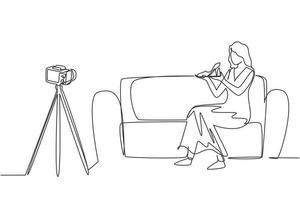 Single continuous line drawing stylish beauty blogger is sitting at sofa, reviewing heels shoe in her hands while recording video with digital camera, tripod. One line draw design vector illustration