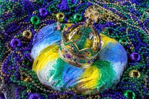 Mardi Gras King Cake topped with crown surrounded by beads and decorations photo