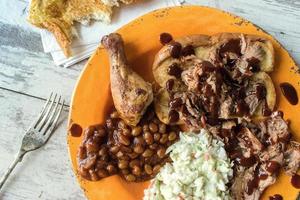 plate of barbecue brisket with chicken leg, baked beans, and coleslaw flat lay photo