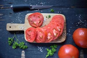 sliced red tomato with salt and herbs flat lay photo