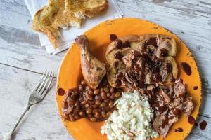 plate of barbecue brisket with chicken leg, baked beans, and coleslaw flat lay photo