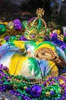 Sliced Mardi Gras King Cake topped with toy baby surrounded by beads and decorations photo