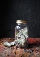 tarro de dinero con monedas y billetes en mesa de madera rústica foto