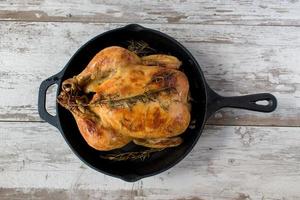 roasted whole chicken with rosemary in cast iron pan flat lay photo