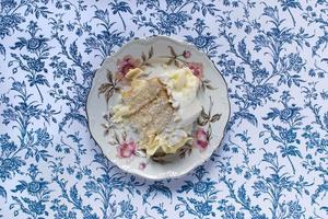 Vanilla cake with white icing cake and slice on blue patterened table photo