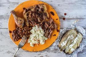 plate of barbecue brisket with chicken leg, baked beans, and coleslaw flat lay photo