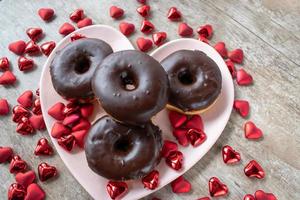 donuts cubiertos de chocolate en un plato en forma de corazón rodeado de corazones de San Valentín foto