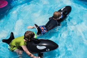 two boys riding swim floats in pool with goggles photo