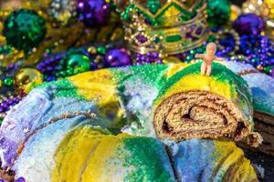 Sliced Mardi Gras King Cake topped with toy baby surrounded by beads and decorations photo