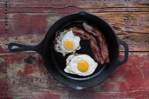 cast iron pan with two fried eggs and bacon flat lay photo