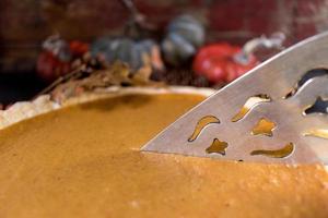 Whole holiday pumpkin pie being cut in fall setting photo