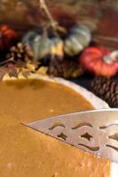 Whole holiday pumpkin pie being cut in fall setting photo