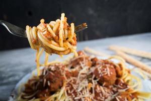 fork wrapped with spaghetti noodles over plate of spaghetti with meatballs photo