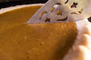 Whole holiday pumpkin pie being cut in fall setting photo