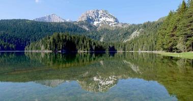 Black Lake in National Park Durmitor in Montenegro. Unesco protected area. Vibrant colors. Reflection of the mountain in the water. Snow in the peaks. Holidays in nature. Forest around the lake.