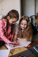 Two girls friends play at home, draw with pencils and felt-tip pens and have fun photo