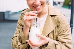 A young woman drinks a milkshake outdoors from a stylish glass jar with a straw photo