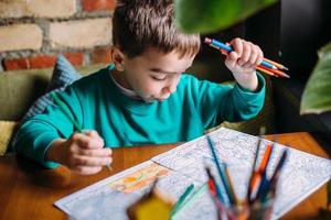 Portrait of a cute happy preschool boy at home or in a cafe draws. photo