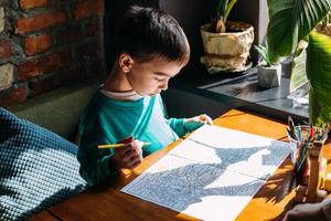 Portrait of a cute happy preschool boy at home or in a cafe draws. photo