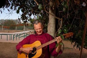 Happy Mature Man singing and playing his acoustic guitar in the park photo