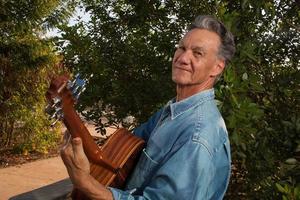 Happy Mature Man singing and playing his acoustic guitar in the park photo