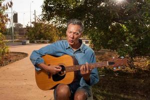 hombre maduro feliz cantando y tocando su guitarra acústica en el parque foto