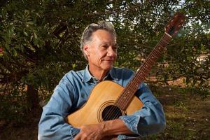 Happy Mature Man singing and playing his acoustic guitar in the park photo