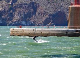 Kite surfing under the Golden Gate Bridge on the San Francisco Bay shown against concrete and orange foundation photo