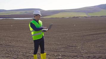 Ingenieur, der in Ackerland arbeitet. ingenieur, der auf erden steht und mit laptop arbeitet. Er macht eine Analyse. er macht sich Notizen auf dem Laptop. moderne und technologische Landwirtschaft. video