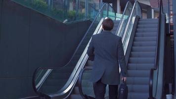 hombre de negocios con bolsa subiendo la escalera mecánica. hombre de negocios subiendo la escalera mecánica mirando su reloj. un hombre de negocios moderno con un maletín. video