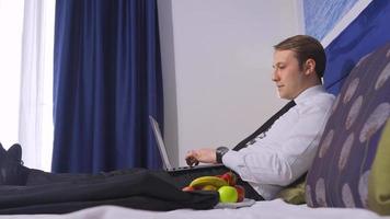 man aan het werk met zijn computer in hotelkamer. fruitschaal. aardbeien eten. man voorbereiden op zakelijke bijeenkomst in hotelkamer. werken op de computer. video