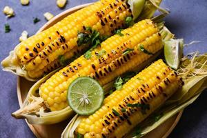 comida de maíz dulce con lima y cilantro, maíz dulce cocinado en el fondo del plato, mazorcas de maíz maduras maíz dulce a la parrilla para comida vegana cena o merienda - vista superior foto