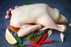 raw duck with spices ready to cook on black background , fresh duck meat on plate for food , whole duck and lemon rosemary chili garlic photo