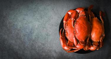 cangrejo fresco en el fondo de la placa negra, cangrejo de marisco cocinando comida hervida o al vapor rojo cangrejo en el restaurante de marisco - vista superior foto