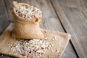 brown rice in the sack with wooden background , raw various rice color mixed thai rice for cooking food , Loonzain rice brown black red white purple health food. photo