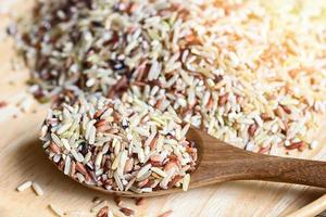 brown rice on wooden spoon , raw various rice color mixed thai rice for cooking food , Loonzain rice brown black red white purple health food. photo