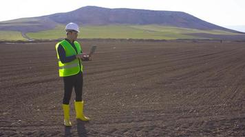 Engineer working in farmland. Engineer standing on earthen land working with laptop. He's doing analysis. He is taking notes on the laptop. Modern and technological agriculture. video
