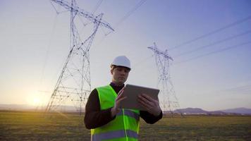 Engineer working in front of power lines at sunset. An engineer with a tablet is working in front of power lines. Conducts field research and investigations. video